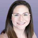 This is a headshot of Megan. Megan is wearing a red shirt and light brown cardigan and is smiling at the camera. Megan has light skin, straight brown hair and wears glasses. The background is a solid, light purple.