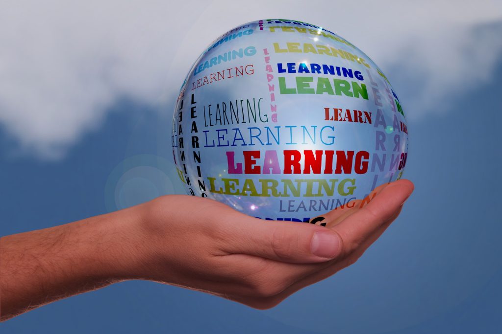 An outstretched hand holds a clear globe with "learning" written in different colors and fonts on it. 