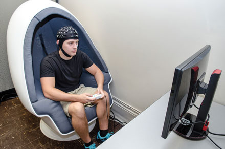 Sitting in the “egg chair,” kinesiology senior Anthony Weiss wears an EEG cap used to measure brain activity while playing a game that measures mental skills such as the ability to stay focused.