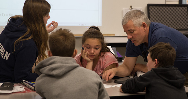 Dean Hanton works with students at their desks in the classroom. 