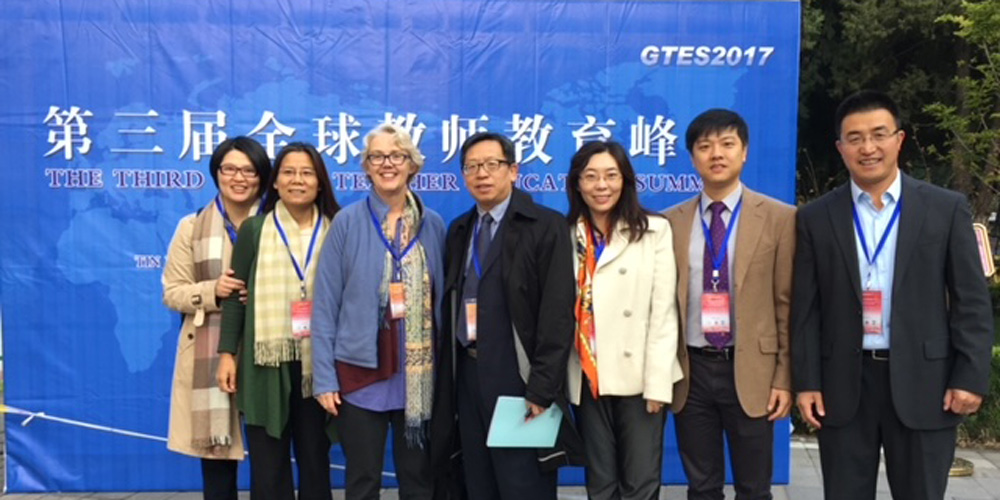 Seven colleagues stand side-by-side in front of a blue banner for a conference in 2017.