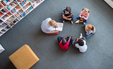 Aerial shot: Students read with a teacher in a library.