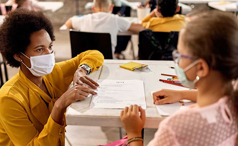 Teacher and student wearing masks collaborate on a lesson.