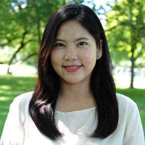 Jungmin Kwon smiles for the camera, foliage in bright green behind her. She wears a white blouse. Her dark hair falls just past her shoulders.