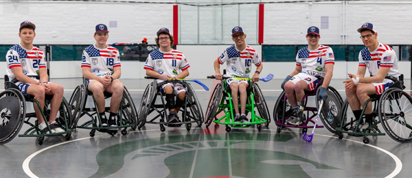 Six Spartans in wheelchair floorball equipment smile for the camera in an MSU sports facility
