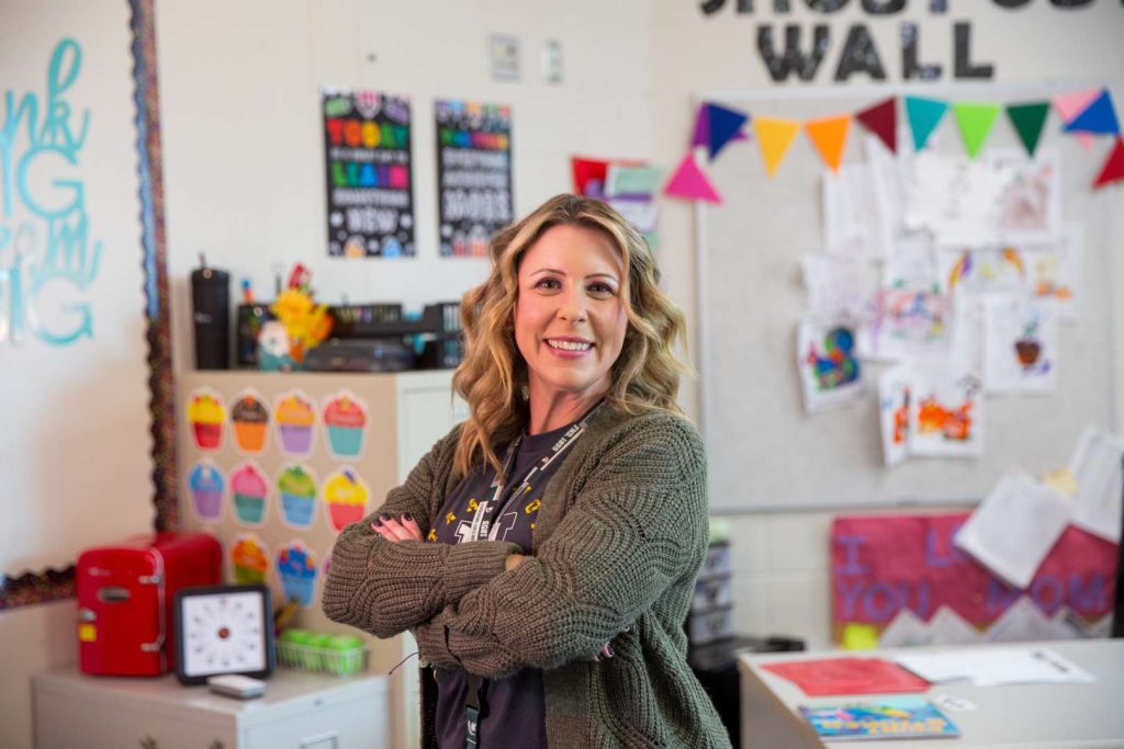 Lindsay standing in classroom smiling a camera with her arms crossed.