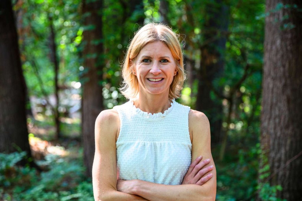 A blonde-haired woman standing outdoors facing camera with her arms crossed