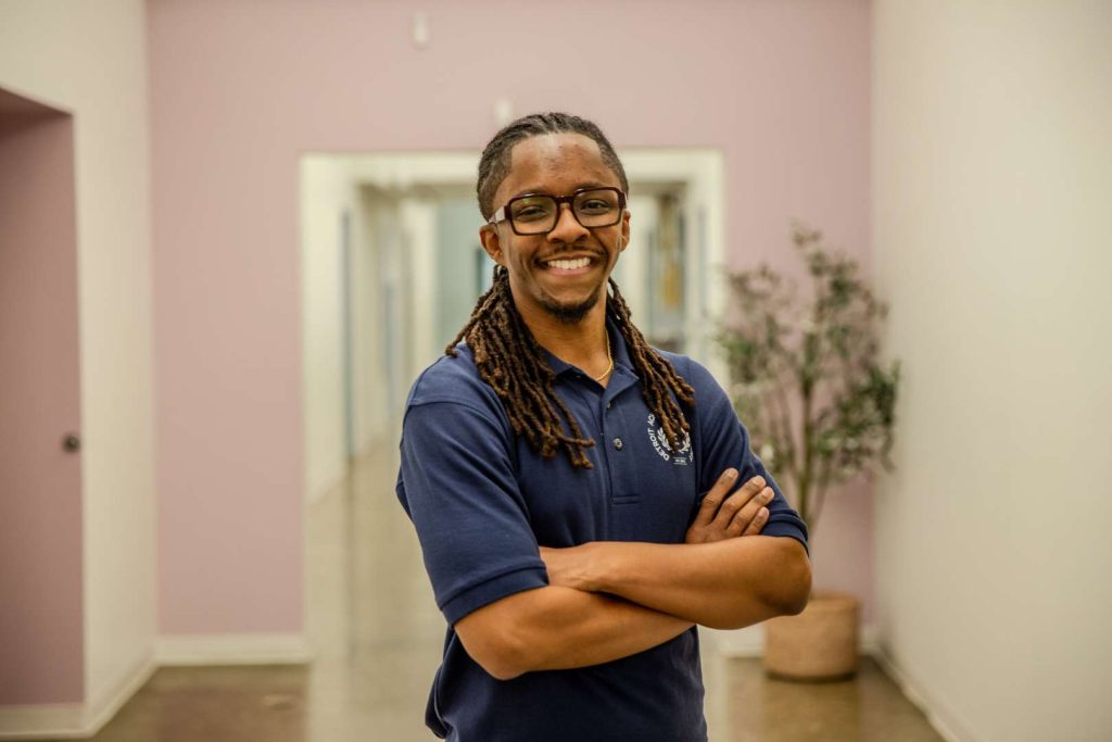 Mario Lemons stands in the hallway of his classroom with his arms crossed.