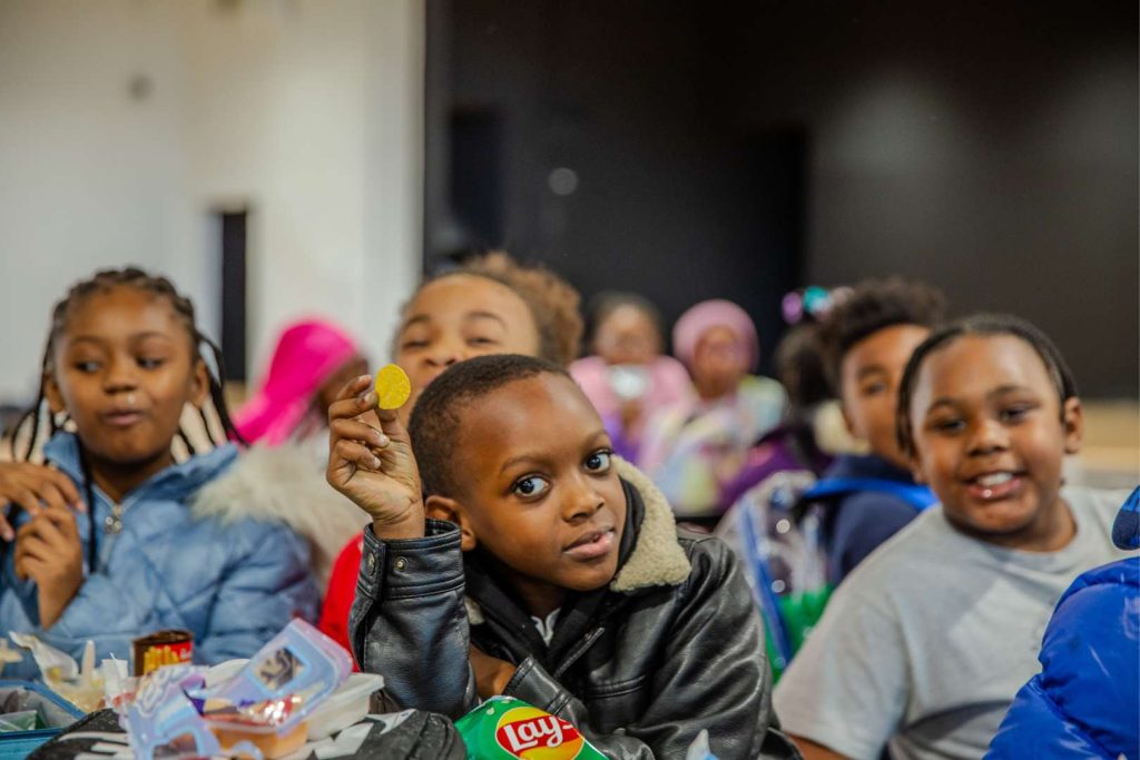 A student in the lunch room shows off his potato chip to the camera.