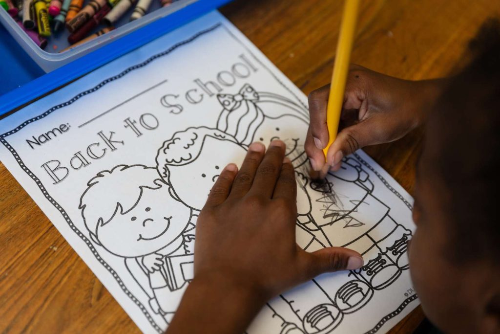 A student coloring on a sheet of paper at their desk.