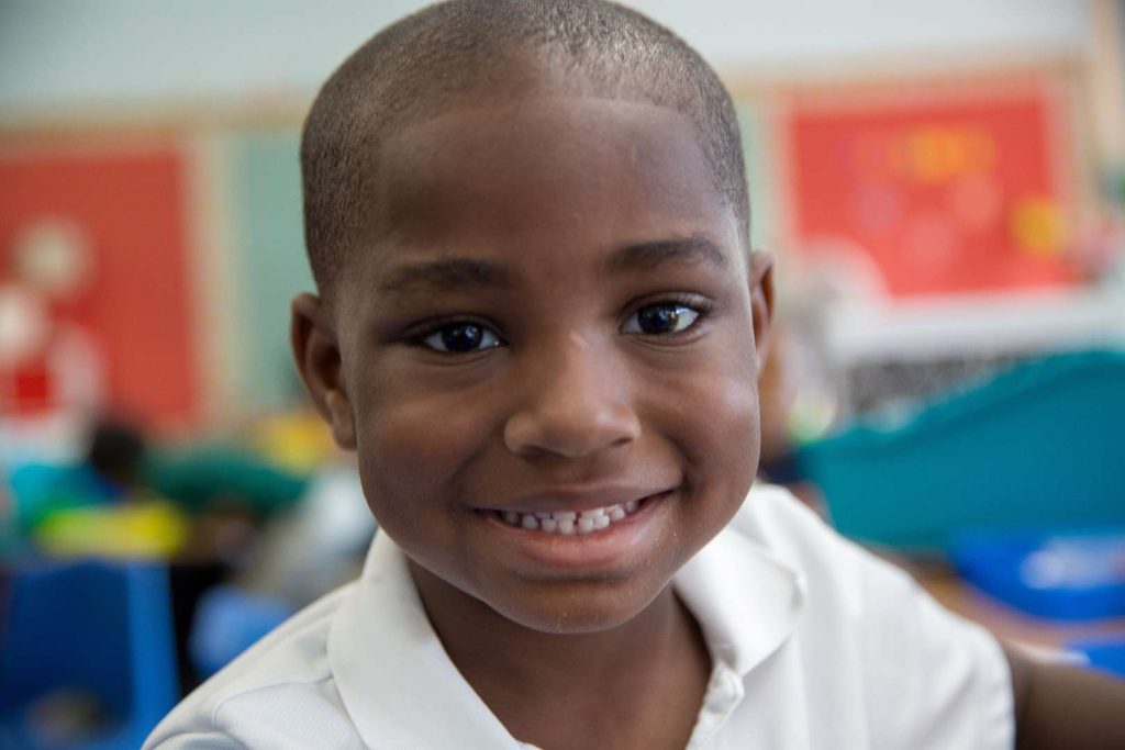 Boy wearing a white polo shirt smiling at camera.