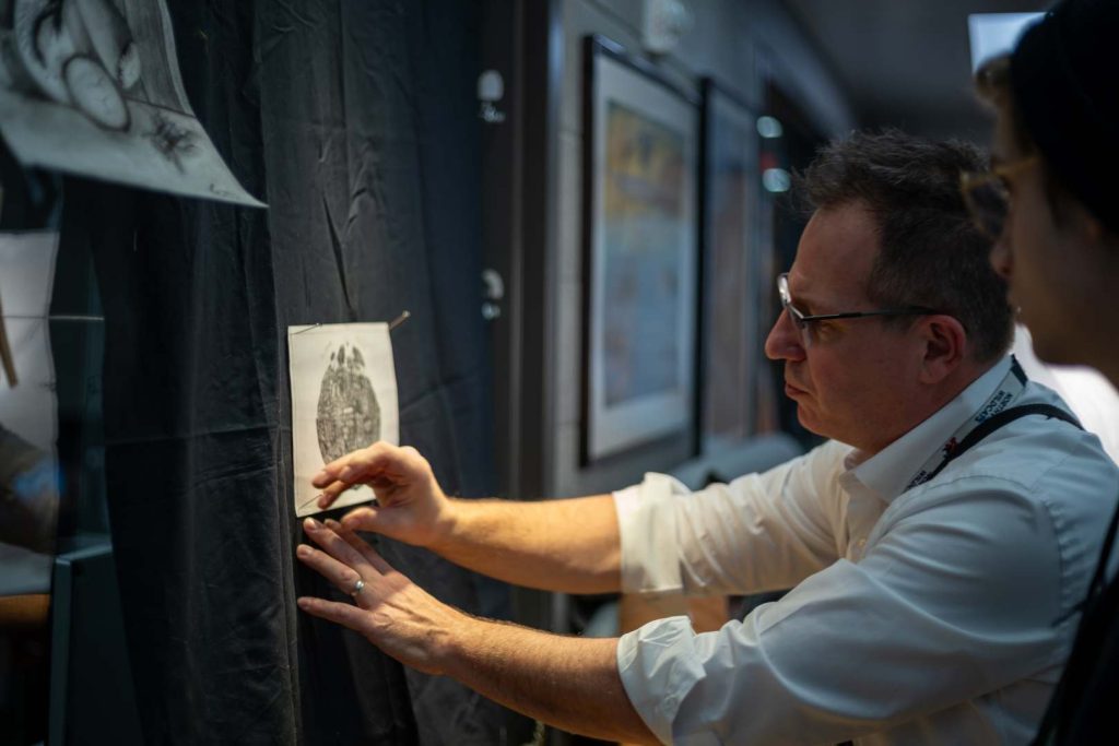 Nathan Kukla pinning a piece of artwork on the wall alongside a student. 