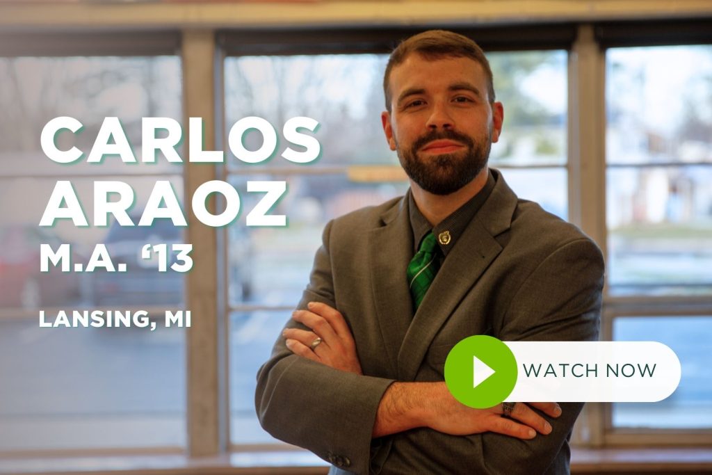 Carlos Araoz stands in classroom smiling at camera with arms crossed.