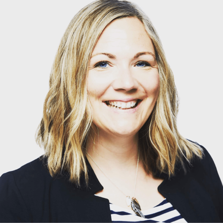 This is a headshot of Mary Wever. Mary is smiling and facing the camera. She has shoulder length blond hair and light skin. She is wearing a black jacket and black and white striped shirt. The background is a solid white.