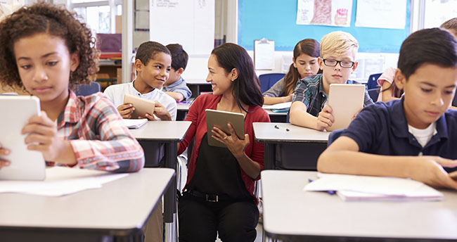 Teacher among kids with computers in elementary school class