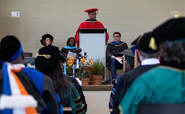 Jackson stands at a podium during a convocation ceremony, in which all doctoral degree recipients are hooded. 