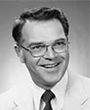 Black and white photo of B. Bradley West. West is wearing a light colored suit jacket, light colored shirt and a dark tie. He also is wearing glasses. Bradley is smiling. 