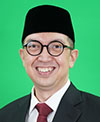 Iwan Syahril smiling. He is wearing a dark suit jacket, white shirt and dark red tie. He also is wearing glasses and a cap that is black. 