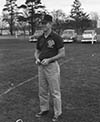 Black and white photo of Willard E. Kenney. He is wearing a polo and a baseball cap whole standing on a sports field. 