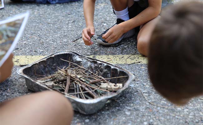 A small metal container filled with twigs and sticks in the center of the photo, with students out of focus around the container. 