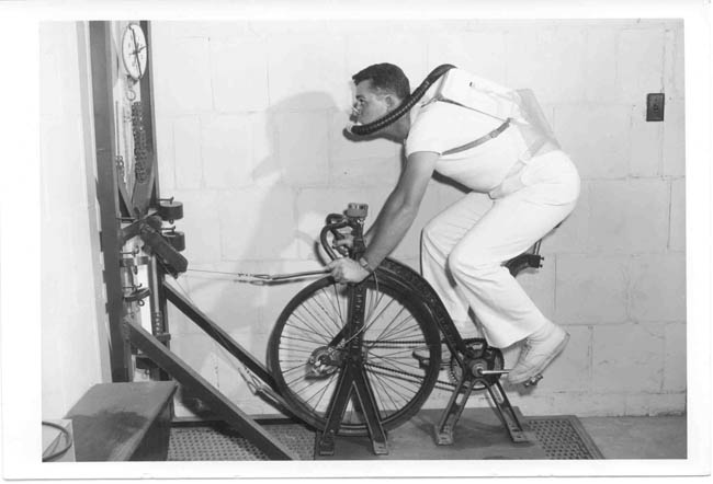 A man cycling on a stationary bike with attached measurement instruments.