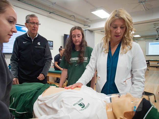 Medical simulation lab with instructors and students practicing on a mannequin.