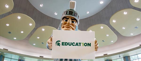 sparty holding spartan education sign