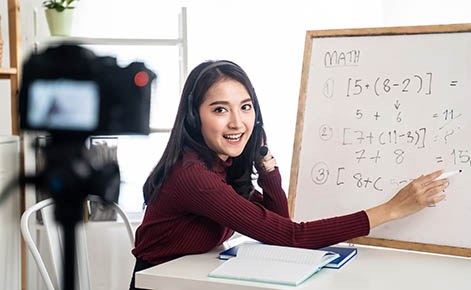 Woman teaching math on whiteboard while on camera.