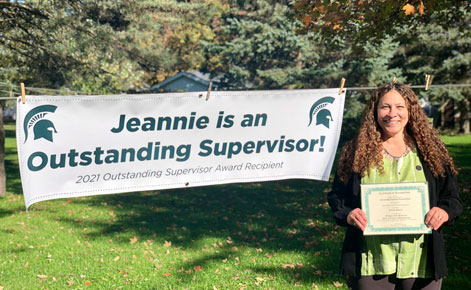 Jeannie Patrick stands outside by a sign announcing her award as Outstanding Supervisor.