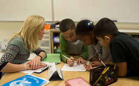 Student teacher helping three children complete an assignment in the classroom.
