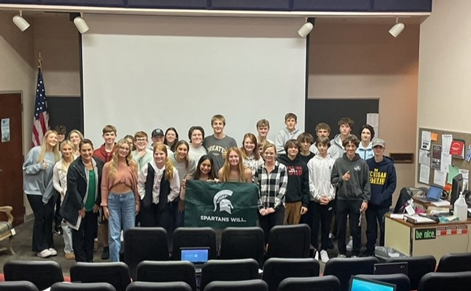A group of students in Rockford Public Schools hold up a Michigan State University sign with the words "Spartans Will"