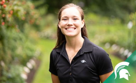Corinne Hobbs smiling at camera wearing black polo shirt. She is standing outdoors on a spring day. 
