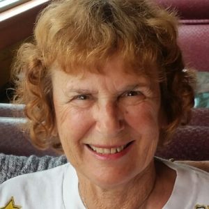 Joy Efron smiles toward the camera. Joy has a white blouse. Joy has curly, auburn-colored hair, cropped short, about chin-length.