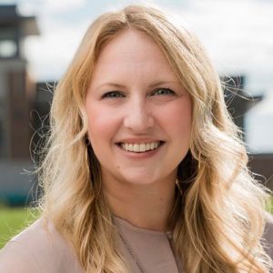 Lauren Jasinski headshot. Lauren smiles in an outdoor photo. Lauren wears a beige blouse and a gold necklace. Lauren's hair is long, blonde and wavy, falling past her shoulders.