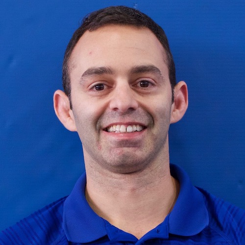 Headshot of Pete Jacobsen. He is wearing a blue polo shit. His dark hair is cropped short. He stands against a blue background.