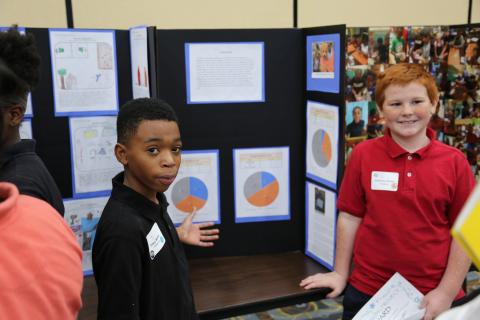 Boys stand in front of poster presenting their scientific findings.
