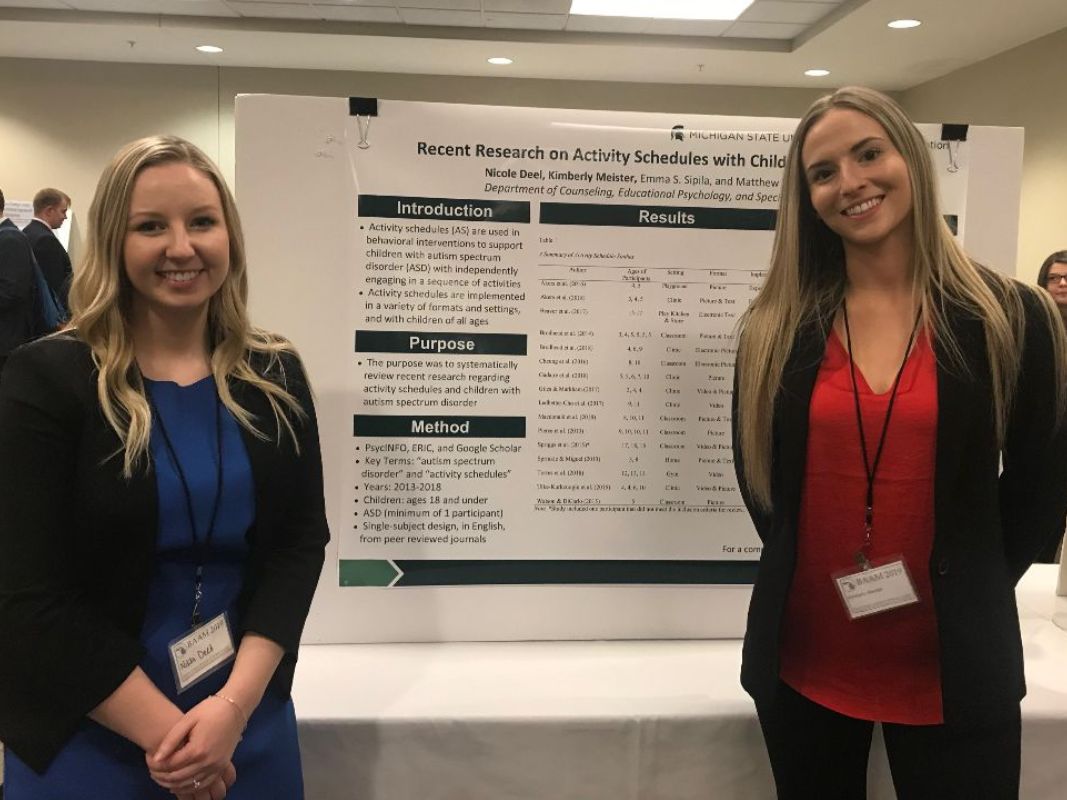 Two women stand in front of a poster presentation.