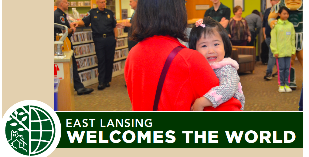 Mother holds a baby in a library setting. Underneath, the title for the event: EAST LANSING WELCOMES THE WORLD.