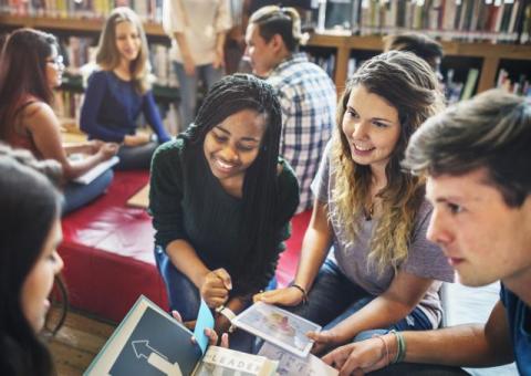 A group of people work together in a library, discussing science books.